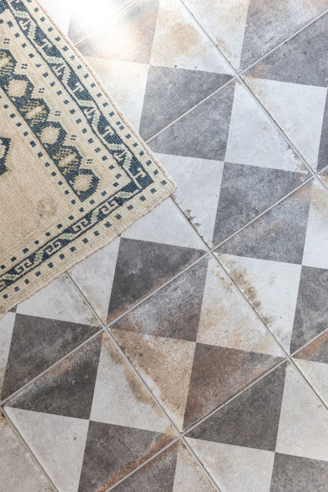Distressed checker floor with tan and blue intricate rug layed on top. 